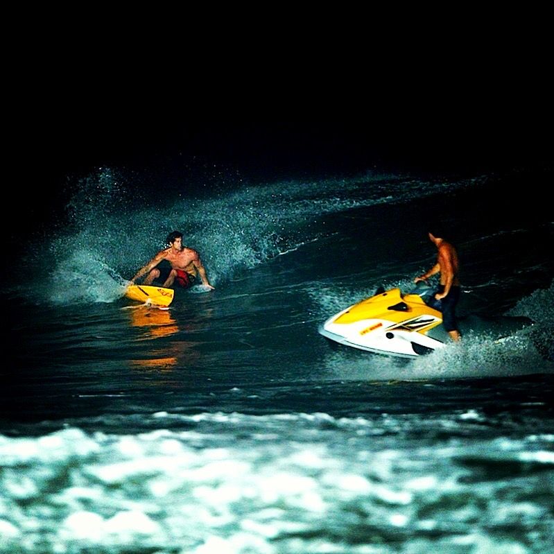 Bruce Irons and Dean Hazza towing into a wave by jet ski under floodlights at the Keramas night surf launch
