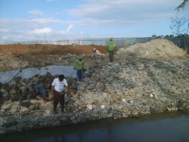 Workers hand-placing rocks into gabion baskets along the river feeding the Keramas surf break