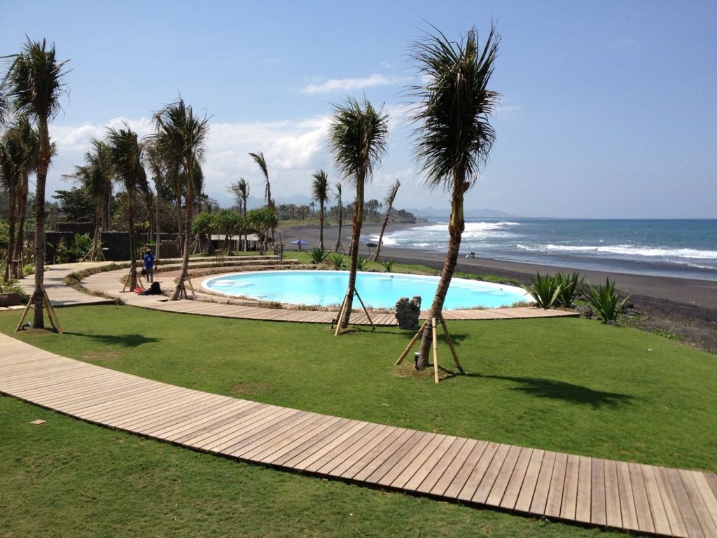 Palm trees being planted around the Hotel Komune beach club pavilion during construction, with the Keramas shoreline behind