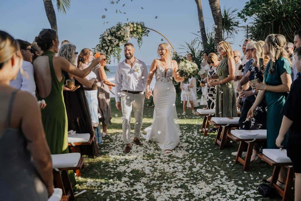 Kayla & Pete walk down the aisle. Guests throw flower petals.